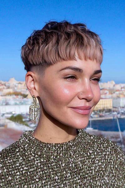 A woman with a textured undercut pixie hairstyle featuring short, choppy layers on top and closely shaved sides.