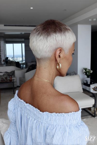 A woman with platinum blonde hair is sporting an undercut pixie hairstyle, featuring closely cropped sides and back with slightly longer hair on top.
