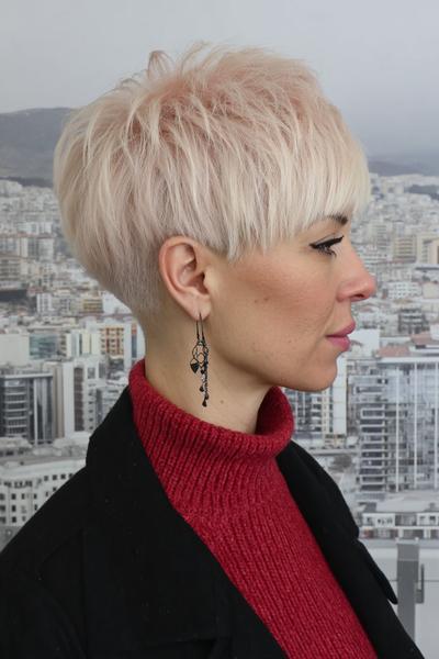 A woman with platinum blonde hair is sporting an undercut pixie hairstyle, featuring closely cropped sides and back with longer, textured layers on top.