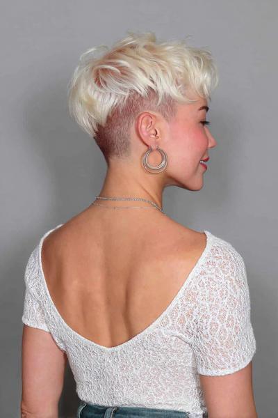 A woman with platinum blonde hair wears an undercut pixie hairstyle, featuring closely shaved sides and back with longer, textured layers on top.