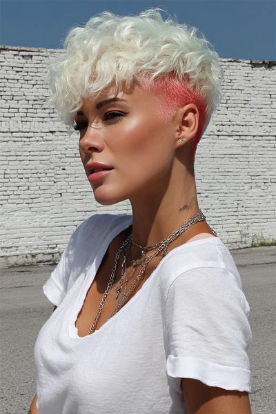 A woman with a curly, platinum blonde pixie cut featuring a sharp undercut dyed bright pink on the sides.