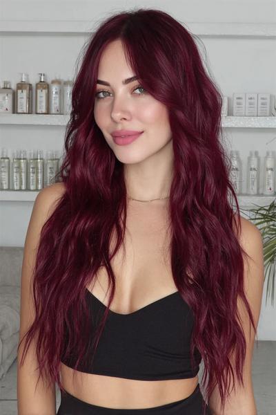 A woman with long, wavy, deep red hair styled with a centre parting is standing indoors, wearing a black crop top.