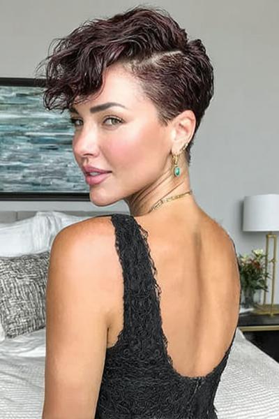 A woman with an undercut pixie hairstyle featuring short, closely cropped sides and longer, wavy hair styled on top.