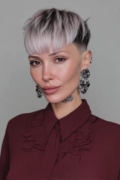 A woman with a short, undercut pixie hairstyle featuring textured, light blonde hair on top and darker shaved sides.