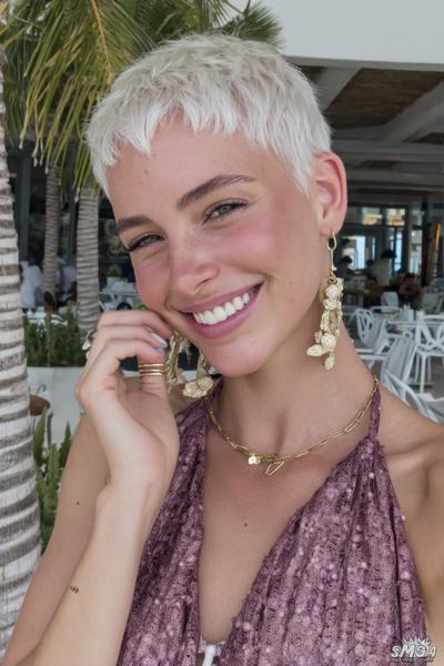 A woman with platinum blonde hair sports a textured undercut pixie hairstyle featuring choppy, uneven fringe and closely cropped sides.