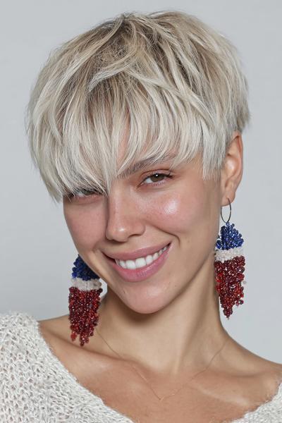 A woman with a textured, platinum blonde undercut pixie hairstyle featuring choppy layers and a long, side-swept fringe.