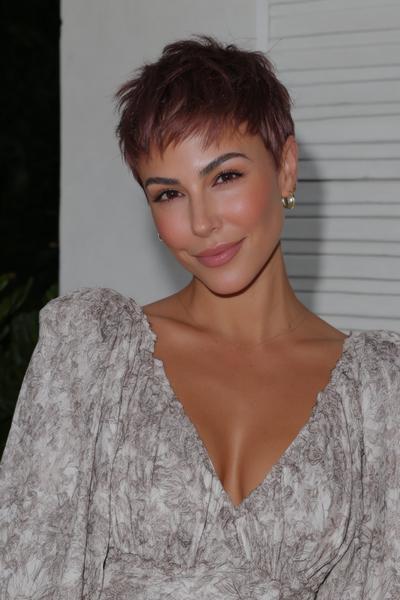 A woman with a textured, short undercut pixie hairstyle featuring choppy layers and soft fringe sweeps her hair forward.