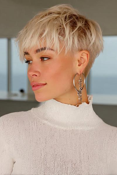 A woman with a textured, platinum blonde undercut pixie hairstyle is shown, with closely cropped sides and longer, tousled layers on top.