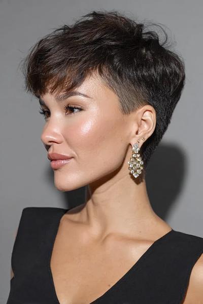 A woman with a dark, textured pixie cut featuring a voluminous top and closely shaven undercut sides.