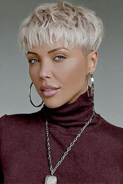 A woman with platinum blonde hair styled in a textured undercut pixie cut, featuring choppy layers on top and closely cropped sides.