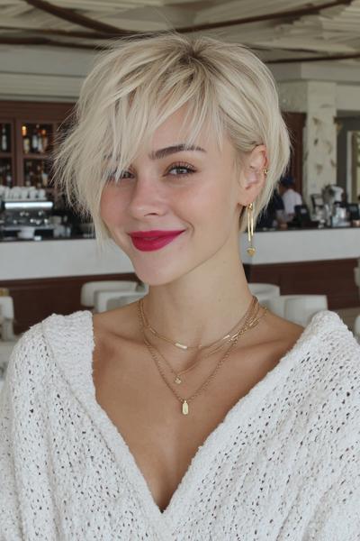 A woman with a textured, platinum blonde undercut pixie hairstyle featuring longer, tousled layers on top and shorter sides.