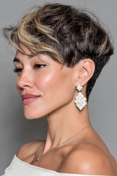 A woman with an undercut pixie hairstyle featuring short, dark hair at the back and sides with longer, tousled layers on top highlighted with blonde streaks.