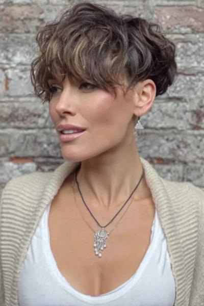 A woman with a textured, wavy undercut pixie hairstyle featuring longer layers on top and shorter, closely-cropped sides.