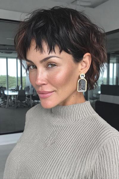 A woman with a textured, wavy undercut pixie hairstyle featuring short, choppy layers and a piecey fringe, styled in a modern and effortless look.
