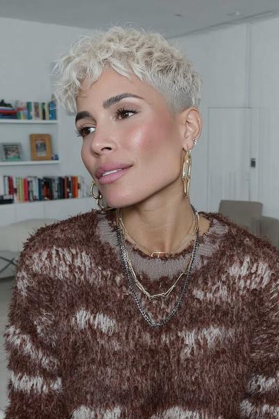 A woman with a short, platinum blonde undercut pixie hairstyle featuring textured curls on top and closely shaved sides.