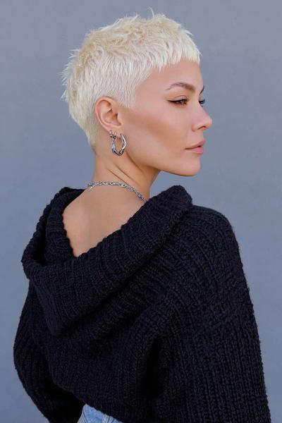 A woman with platinum blonde hair wears an undercut pixie hairstyle, featuring closely cropped sides and back with slightly longer, textured layers on top.