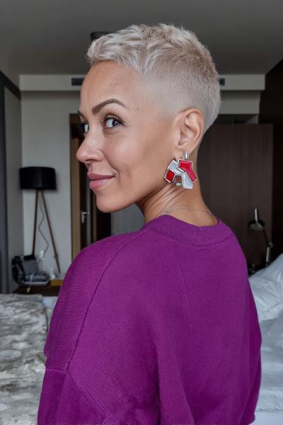 A woman with platinum blonde hair is sporting a textured undercut pixie hairstyle, featuring closely cropped sides and back with slightly longer hair on top.