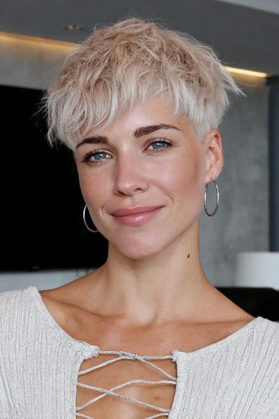 A woman with a textured, platinum blonde undercut pixie hairstyle featuring choppy layers and a slightly tousled fringe.