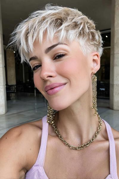 A woman with a platinum blonde undercut pixie hairstyle featuring textured, tousled layers on top and closely cropped sides.