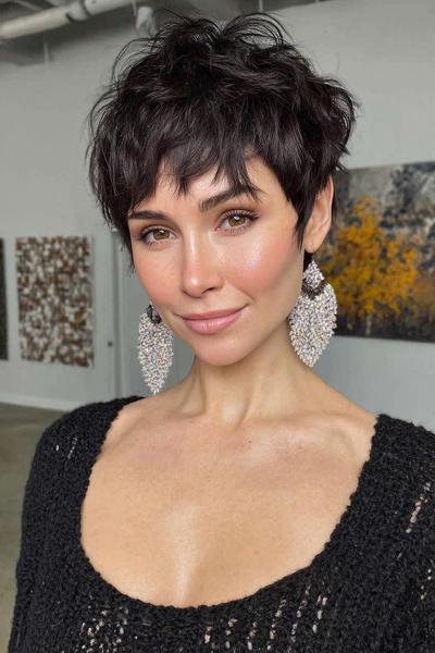 A woman with a textured, dark brown undercut pixie hairstyle featuring short, tousled layers and longer fringe at the front.
