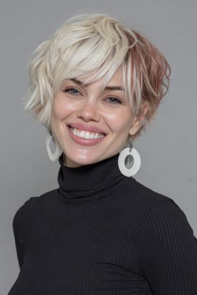 A woman with a textured, tousled undercut pixie hairstyle featuring platinum blonde hair with hints of light pink at the back, styled with long, side-swept fringe.