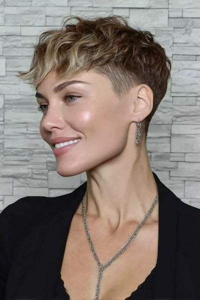 A woman with an undercut pixie hairstyle featuring short, closely cropped sides and back, with longer, softly textured hair on top styled in tousled waves.