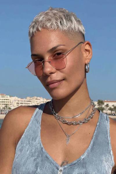A woman with bleached blonde hair is wearing a textured, closely-cropped undercut pixie hairstyle with faded sides.