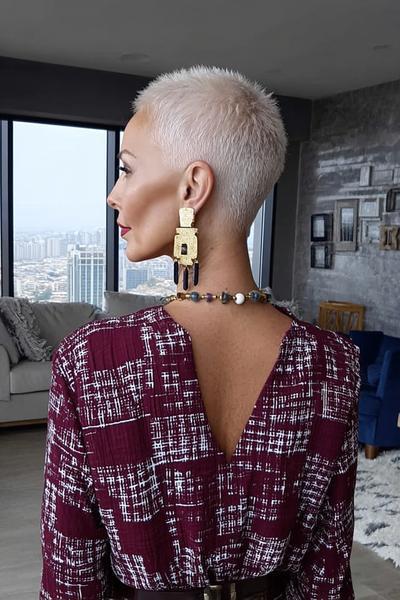 A woman with a platinum blond undercut pixie hairstyle is shown from behind, featuring very short, closely-cropped sides and back with slightly longer textured hair on top.