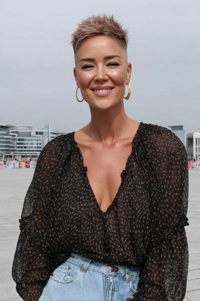 A woman with a short, textured pixie cut featuring a closely shaved undercut on the sides and back, with longer, tousled hair on top.