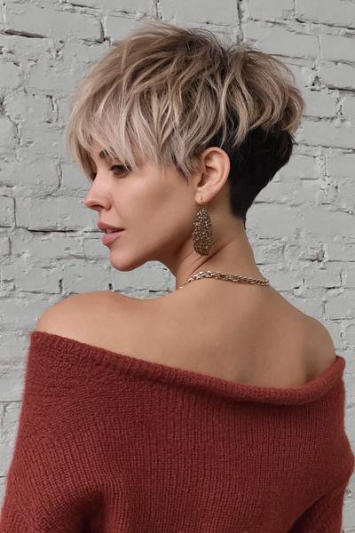 A woman with a textured, layered pixie cut featuring a voluminous, light blonde top and a dark, closely cropped undercut at the back.
