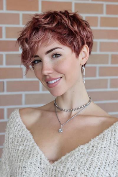 A woman with a textured, rose gold undercut pixie hairstyle featuring tousled layers and a soft side fringe.