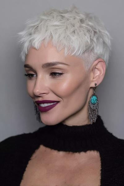 A woman with an icy blonde textured undercut pixie hairstyle, featuring very short, closely-cropped sides and longer, tousled layers on top.